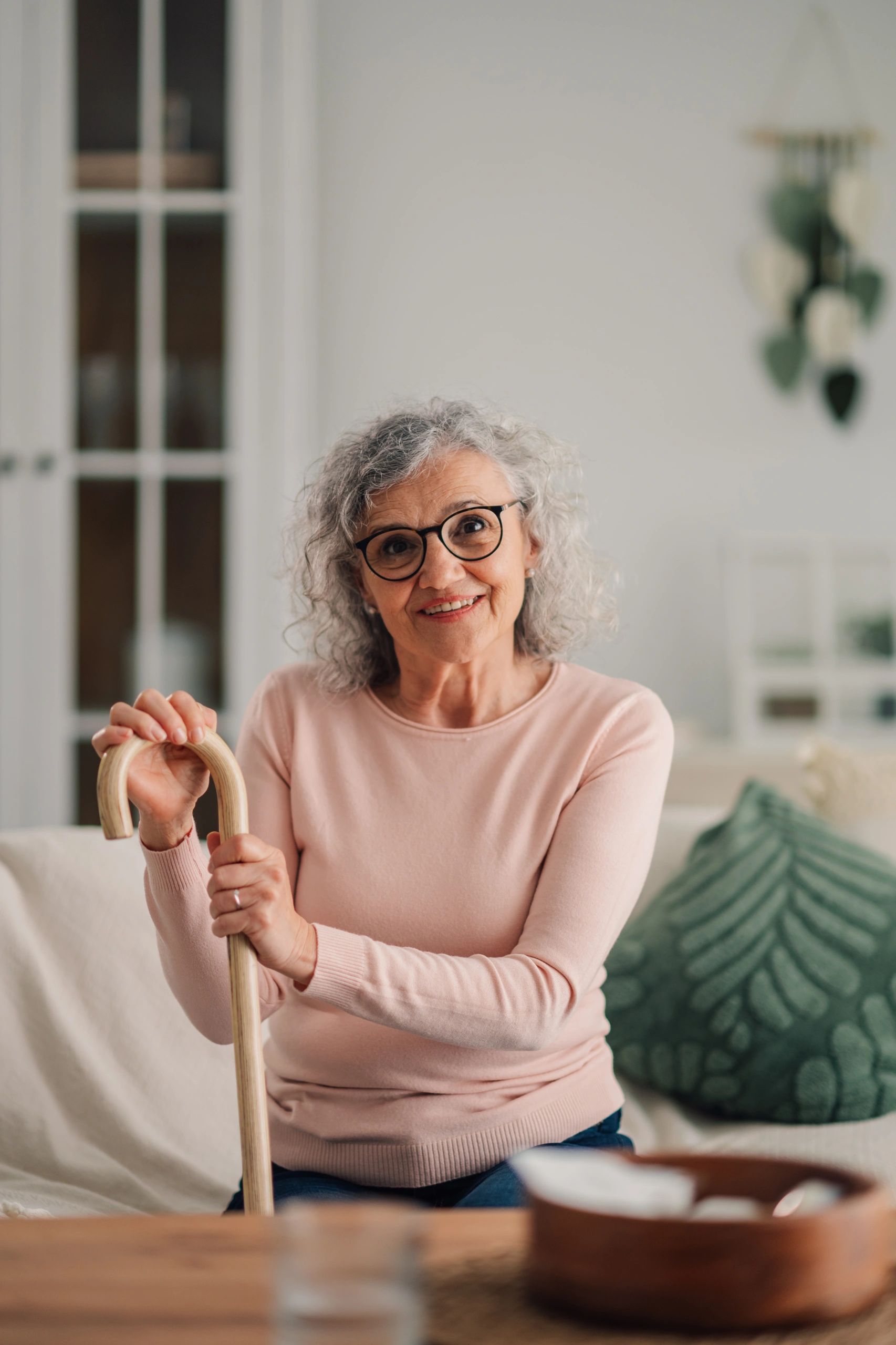 Senior woman with gray curly hair smiling while holding a walking cane